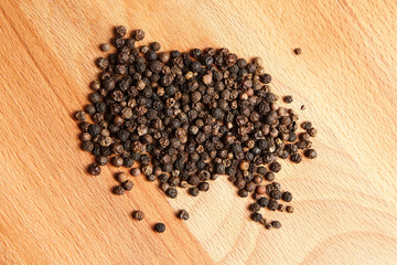 Heap of black peppercorns on  wooden beech cutting board