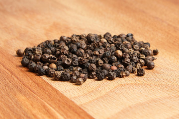 Heap of black peppercorns on  wooden beech cutting board