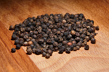 Heap of black peppercorns on  wooden beech cutting board