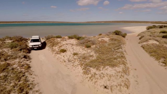 An aerial shot of a coast and sea with a ute driving on lands