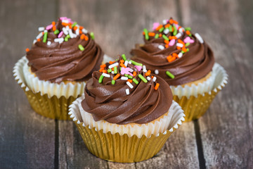 Cupcakes decorated with creamy chocolate frosting and sprinkles on rustic wooden table 
