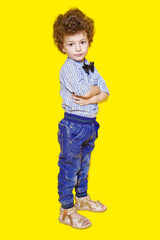 A little boy with hands folder looking with displeasure at the camera on a yellow background