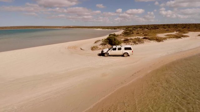 An aerial shot of a coast and sea with a ute driving on lands
