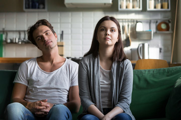 Lazy millennial couple getting bored at home sitting on sofa, young funny disinterested girl and...