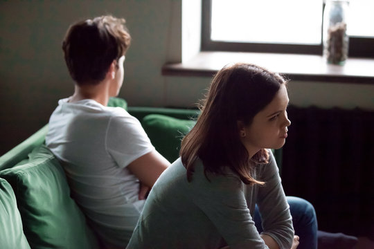 Disappointed frustrated millennial girlfriend and boyfriend avoiding each other offended after argument, resentful young couple sitting on sofa not talking feeling insulted and misunderstood concept