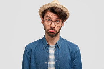 It`s pity! People and resentment concept. Offended bearded male gardener curves and purses lips, looks with displeased sorrowful expression, disconetent with harvest, wears straw summer hat.