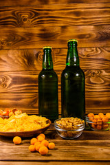 Two bottles of beer and different snacks on wooden table
