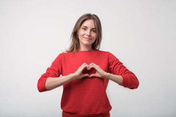 Cute beautiful caucasian girl dressed in red t-shirt in love making heart with fingers and smiling
