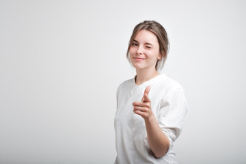 Positive cheerful young caucasian woman wearing white casual T-shirt blinking her eyes and smiling...