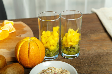 on the wooden table are two glasses of fruit smoothies. next door is a cup with cereal and fresh fruit. horizontal photo.