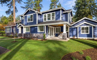 Beautiful luxury home exterior on sunny day with green grass, blue sky, and backdrop of trees - Powered by Adobe