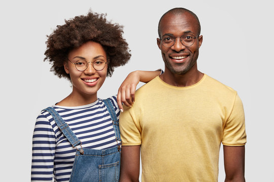 Horizontal shot of pleased young African American man and woman have gentle smiles, show good relationships, have pleasant talk together, feels support from each other, isolated on white background