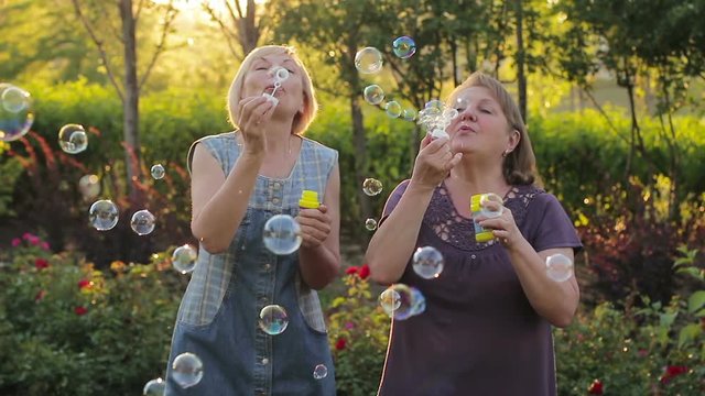 Two elderly women blowing bubbles. Elderly female friends having fun in the park together
