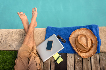 Man relaxing near swimming pool with computer
