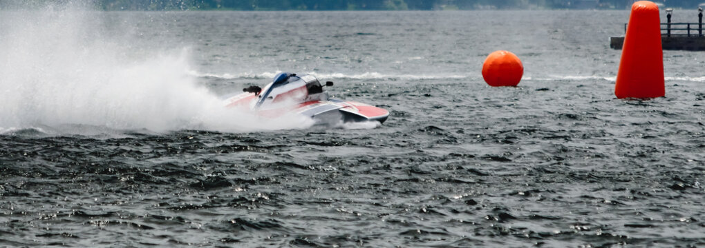 Red and white hydroplane racing boat on river heading towards orange bouys.
