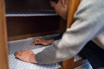 Man placing protective liner sheet inside on wooden cabinets with hands, pricking with pin in...
