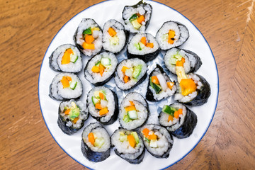 Flat top closeup of handmade homemade maki California vegetable sushi pieces plain with white rice, orange bell pepper, marinated green cucumbers, avocado on plate
