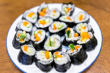 Closeup of handmade homemade maki California vegetable sushi pieces plain with white rice, orange bell pepper, marinated green cucumbers, avocado on plate