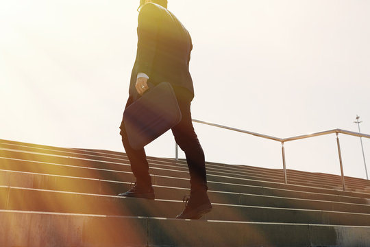 Young confidental businessman wearing suit and running fast upstairs. Horizontal outdoors shot.Sunny effect