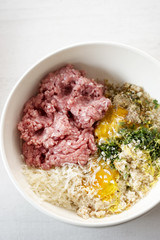 Meatballs ingredients in the bowl. Minced pork meat, seasoning, herbs, breadcrumbs, egg yolk, parmesan cheese. 