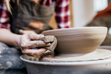 Female potter making clay pottery on a spin wheel.