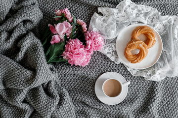 A cup of coffee with sweets and peonies on a gray background