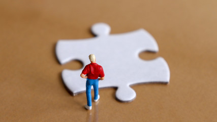 A miniature man looking down at a piece of the puzzle.