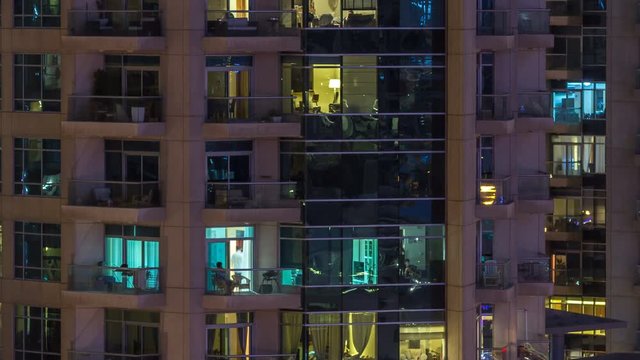 Windows of the multi-storey building of glass and steel lighting inside and moving people within timelapse