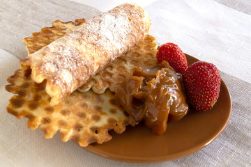 Waffles of thin dough with chocolate paste and ripe strawberries, laid on a round brown saucer.