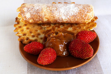 Waffles made from homemade dough, laid on a brown saucer with chocolate pasta and red strawberries.