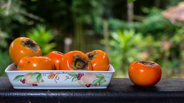 red Persimons (khaki) in ceramic bowl against tropical background