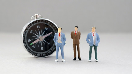 Three miniature men standing in front of the compass.