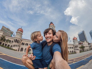 Fototapeta na wymiar happy family makes selfie on the background on background of Merdeka square and Sultan Abdul Samad Building. Traveling with children concept