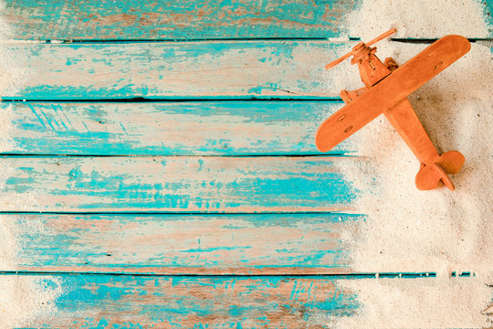 Have a vacation and travel in summer concept - top view of beach sand and toy air plane on wood plank in blue sea paint background.
