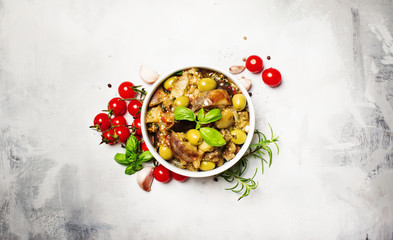 Stewed aubergines with vegetables and herbs in a bowl, light background, top view