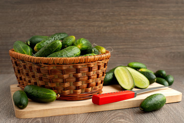 Cucumbers in a basket and on a cutting board. Many cucumbers in a wicker basket on a wooden background. Sliced cucumbers on a cutting board. Preparation of vegetables.