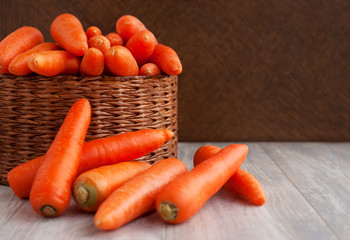 Carrots in a basket. A lot of carrots in a large wicker basket on a wooden background. Orange vegetables.