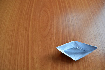 Origami a paper ship from a empty white blank sheet in a cell in corner of wide wooden table. Top...