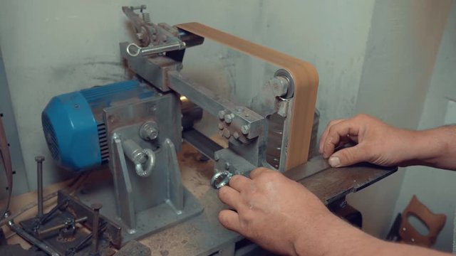 Craftsman sharpening knife blade on professional grinder lathe in workshop. DIY knife making