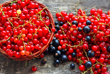 Berries of black and red currants lie in the basket and on the wooden surface.