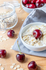 Diet and healthy Breakfast: oatmeal with cherries in a white plate on a gray tablecloth, in the background dish with cherries and a can of oatmeal