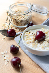 Diet and healthy Breakfast: oatmeal with cherries in a white plate on a gray tablecloth, in the background dish with cherries and a can of oatmeal