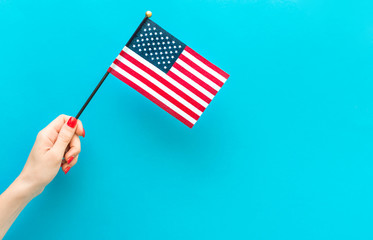 Woman's hand holding small american flag on blue background. Space for text.