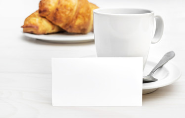 Blank card with cup of coffee and croissants on the white wooden table. Copy space.