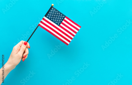 Woman's hand holding small american flag on blue background. Space for text.