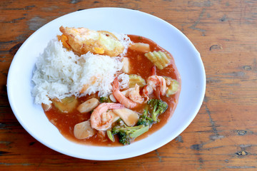 stir fried shrimp and Broccoli in thai red curry paste sauce with rice, Curry fried shrimps and cooked rice in white dish closeup on wooden table. Thai style food.
