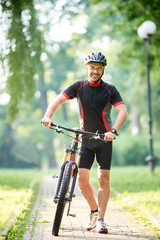 Athletic smiling guy cyclist walking near bike happy to begin morning with training. Sportsman having fun exercising outdoors. Man going to bright future, success. Concept of healthy lifestyle