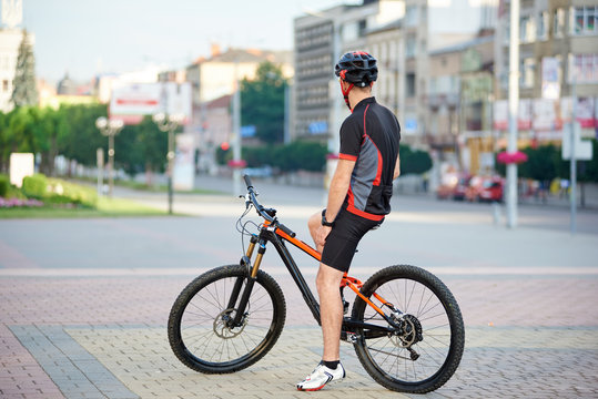 Back view of athletic male bicyclist resting on bicycle after hard race. Sportsman taking break after morning outdoor activities riding bike. Concept of healthy lifestyle, exercising on fresh air