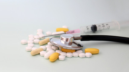 A stethoscope and syringe placed on top of a pill.