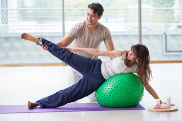 Personal coach helping woman in gym with stability ball